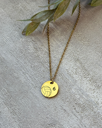 Gold necklace with a volleyball pendant on a textured surface