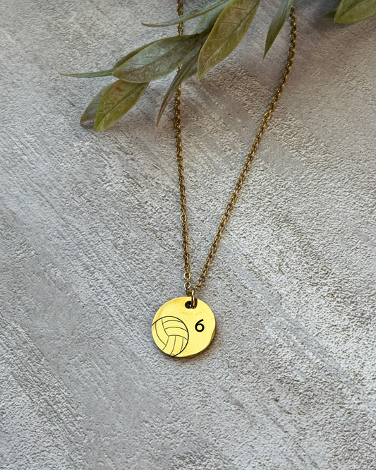 Gold necklace with a volleyball pendant on a textured surface